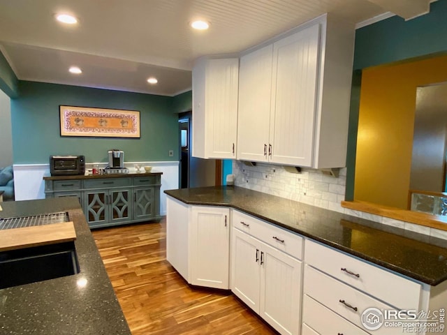 kitchen with ornamental molding, light hardwood / wood-style flooring, white cabinetry, and dark stone counters