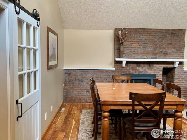 dining room featuring hardwood / wood-style floors, lofted ceiling, a textured ceiling, and brick wall