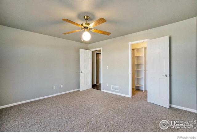 unfurnished bedroom with a walk in closet, ceiling fan, a closet, and carpet floors