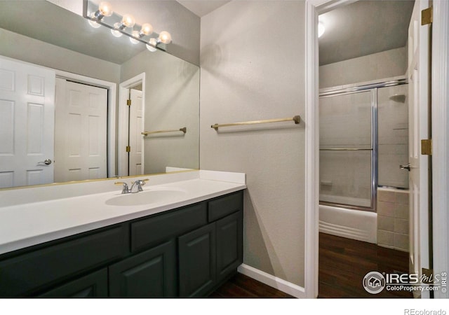 bathroom featuring hardwood / wood-style floors, vanity, and bath / shower combo with glass door