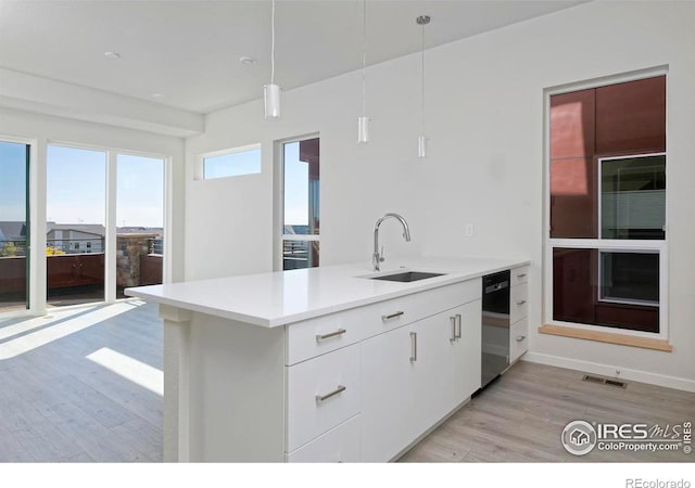 kitchen featuring white cabinets, sink, light hardwood / wood-style floors, kitchen peninsula, and decorative light fixtures