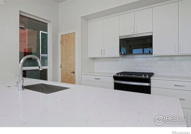 kitchen featuring electric range oven, sink, decorative backsplash, light stone countertops, and white cabinetry