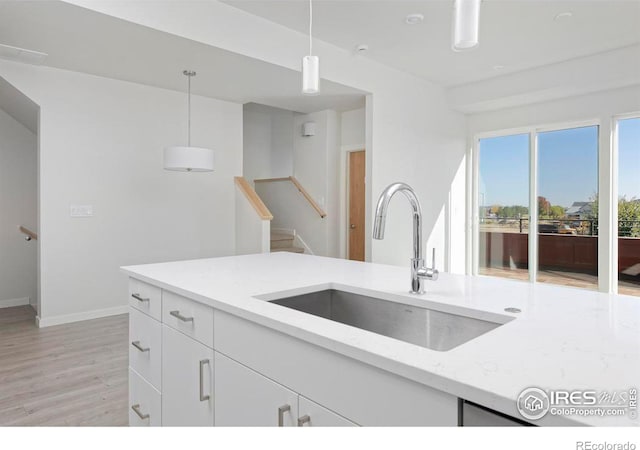 kitchen featuring light stone counters, white cabinets, sink, decorative light fixtures, and light hardwood / wood-style floors