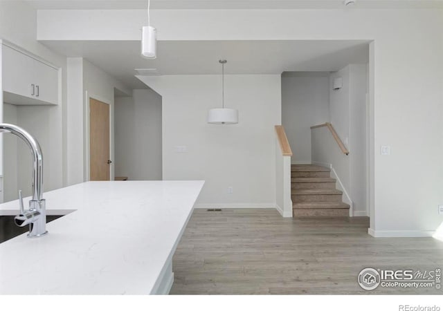 kitchen featuring sink, hanging light fixtures, light hardwood / wood-style floors, and white cabinetry