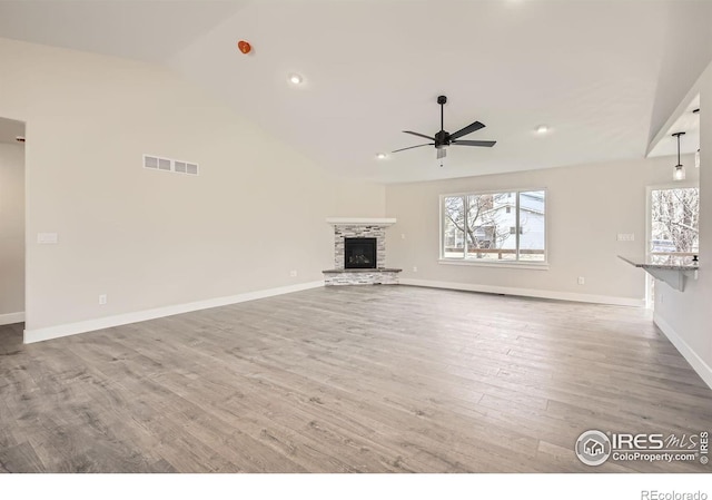 unfurnished living room with ceiling fan, a stone fireplace, wood finished floors, visible vents, and baseboards