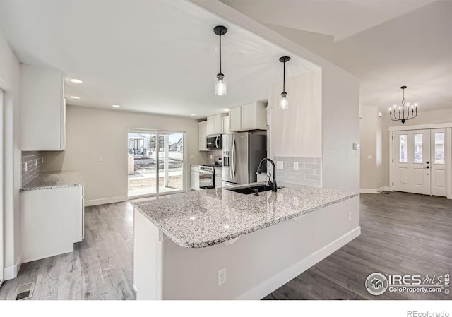 kitchen featuring appliances with stainless steel finishes, white cabinets, hanging light fixtures, and a peninsula