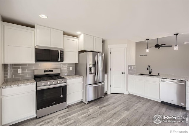 kitchen featuring light stone counters, backsplash, appliances with stainless steel finishes, white cabinetry, and a sink