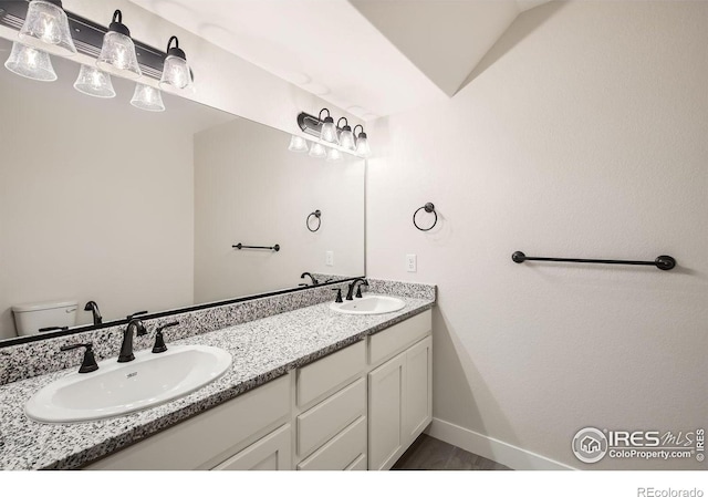 full bath with double vanity, wood finished floors, a sink, and baseboards