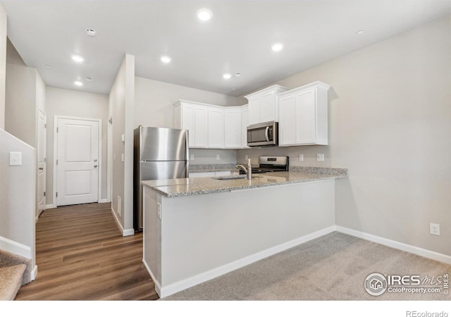 kitchen featuring kitchen peninsula, stainless steel appliances, dark hardwood / wood-style flooring, light stone counters, and white cabinets