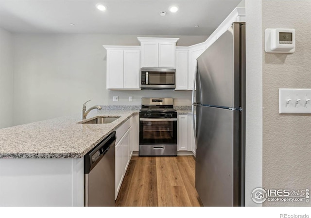 kitchen with light stone counters, light wood-type flooring, white cabinets, sink, and appliances with stainless steel finishes