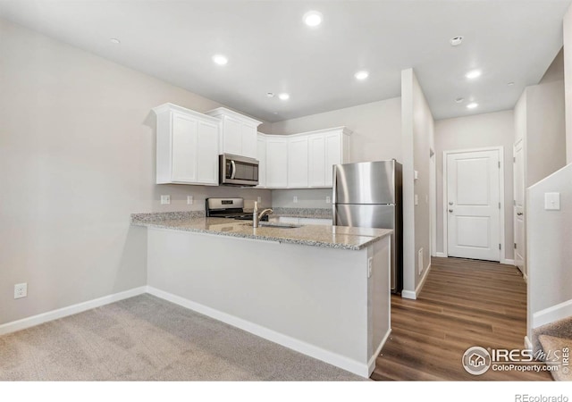 kitchen with light stone counters, dark hardwood / wood-style flooring, kitchen peninsula, white cabinets, and appliances with stainless steel finishes