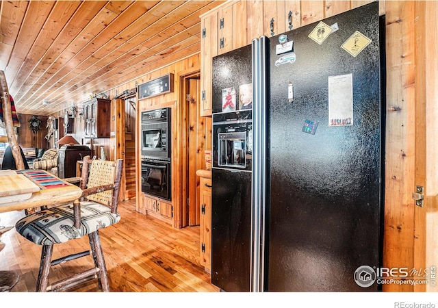 kitchen featuring black appliances, wooden walls, and light wood-type flooring