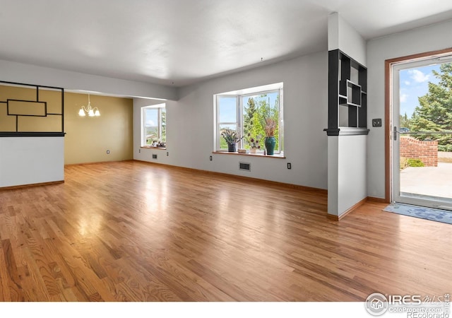 unfurnished living room with light wood-type flooring and an inviting chandelier