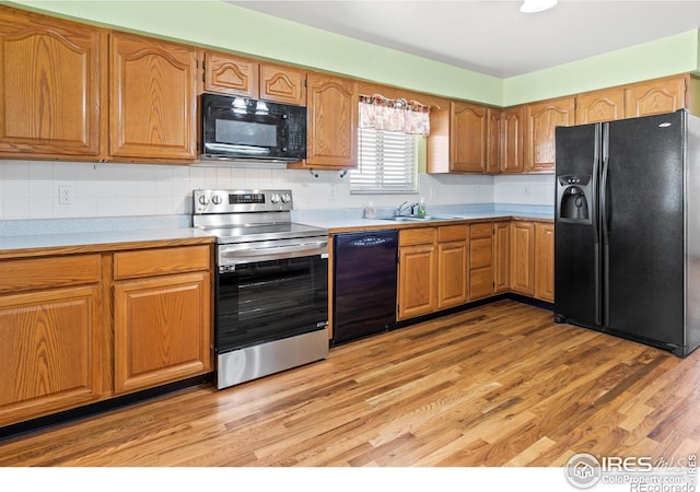 kitchen with black appliances, decorative backsplash, sink, and light hardwood / wood-style flooring