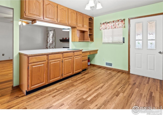 kitchen featuring ceiling fan with notable chandelier, kitchen peninsula, and light hardwood / wood-style flooring