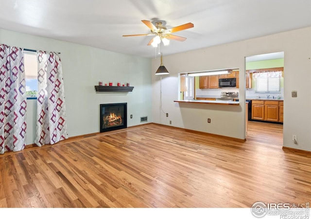 unfurnished living room with ceiling fan, sink, and light wood-type flooring