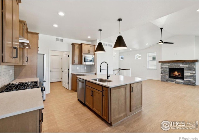 kitchen with stainless steel appliances, vaulted ceiling, sink, a center island with sink, and hanging light fixtures