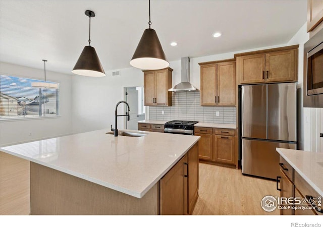 kitchen with sink, wall chimney exhaust hood, decorative light fixtures, a kitchen island with sink, and appliances with stainless steel finishes