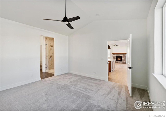 spare room with ceiling fan, a fireplace, light carpet, and vaulted ceiling