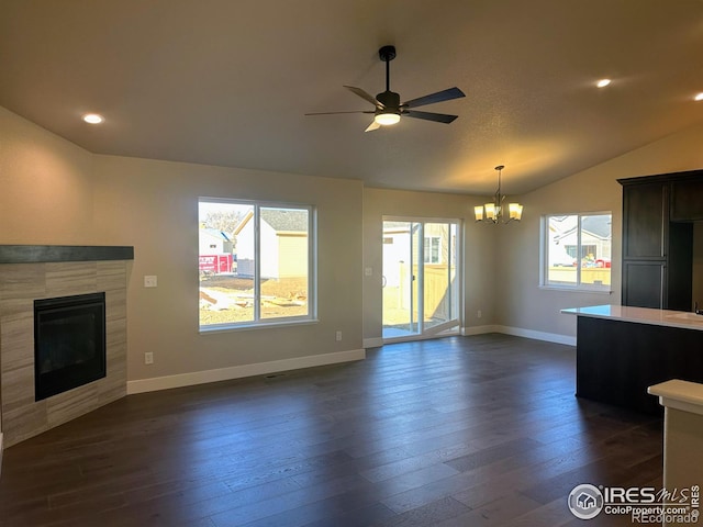 unfurnished living room featuring a tile fireplace, plenty of natural light, dark wood-type flooring, and ceiling fan with notable chandelier