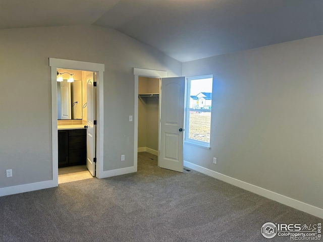 unfurnished bedroom with light carpet, a walk in closet, ensuite bath, a closet, and lofted ceiling