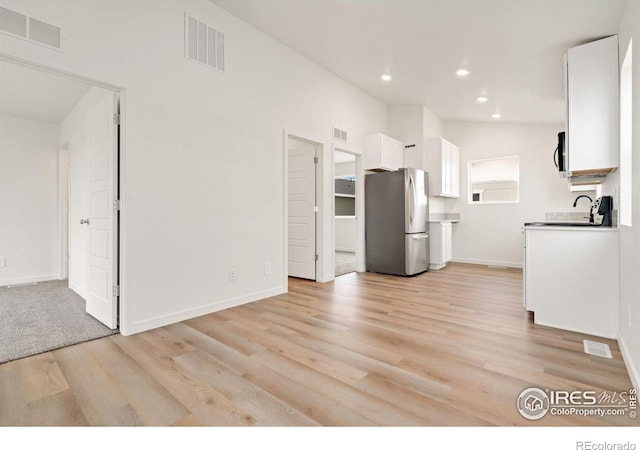 kitchen featuring lofted ceiling, white cabinetry, sink, stainless steel refrigerator, and light wood-type flooring