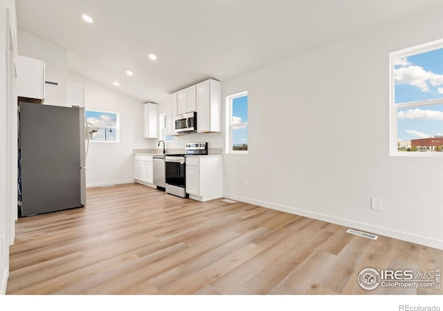 kitchen with white cabinets, vaulted ceiling, appliances with stainless steel finishes, and light hardwood / wood-style floors