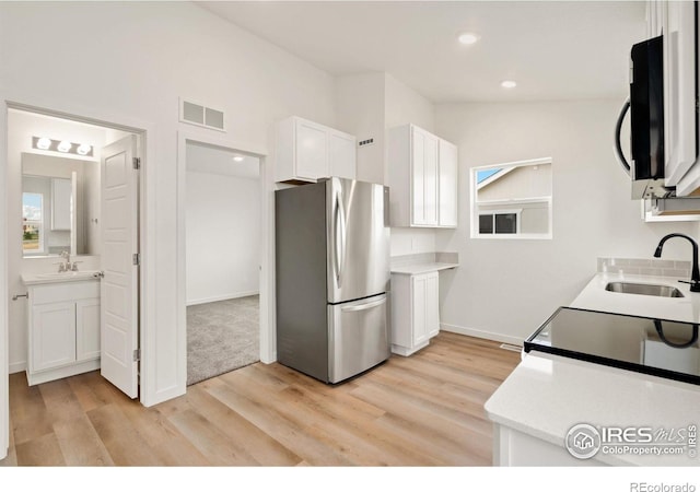 kitchen featuring sink, white cabinetry, stainless steel fridge, and light wood-type flooring