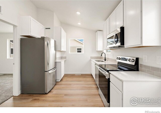 kitchen with appliances with stainless steel finishes, light hardwood / wood-style floors, white cabinetry, and sink