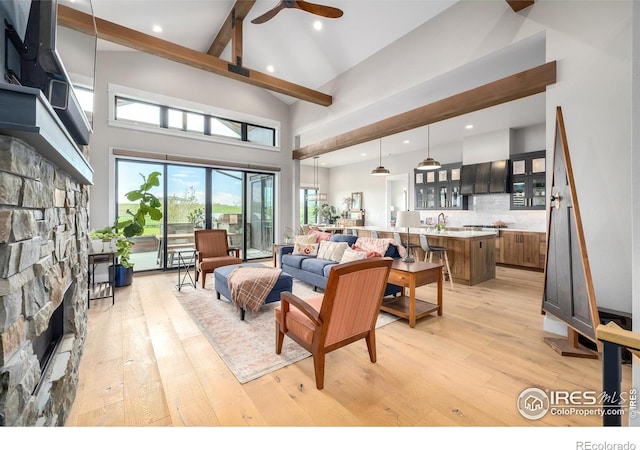 living room featuring a high ceiling, a stone fireplace, ceiling fan, and light hardwood / wood-style floors