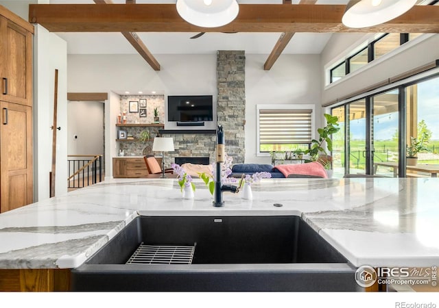 kitchen featuring a stone fireplace, beam ceiling, high vaulted ceiling, and light stone counters