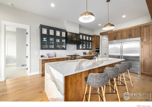 kitchen featuring stainless steel appliances, a center island with sink, light hardwood / wood-style floors, and backsplash