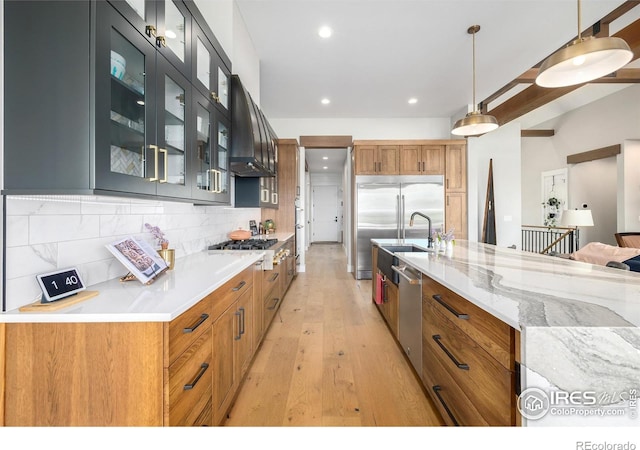 kitchen with light wood-type flooring, appliances with stainless steel finishes, wall chimney exhaust hood, decorative light fixtures, and tasteful backsplash