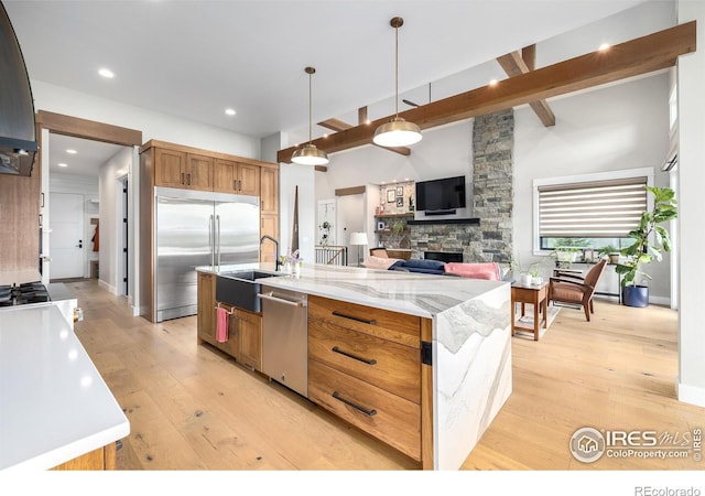 kitchen with decorative light fixtures, light stone counters, light hardwood / wood-style flooring, stainless steel appliances, and beamed ceiling