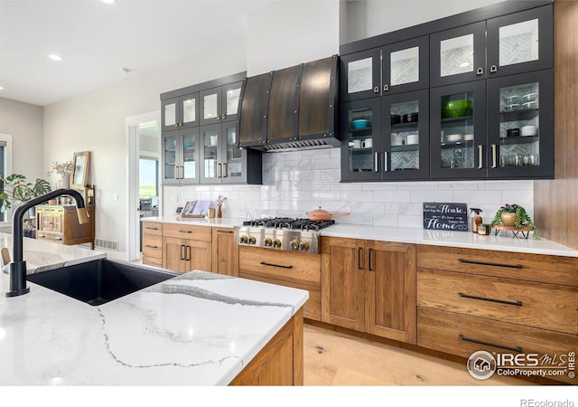 kitchen featuring light hardwood / wood-style floors, light stone countertops, ventilation hood, stainless steel gas cooktop, and tasteful backsplash