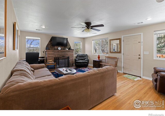 living room with light hardwood / wood-style floors, a textured ceiling, a fireplace, and ceiling fan