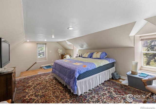 bedroom with vaulted ceiling, wood-type flooring, a textured ceiling, and multiple windows