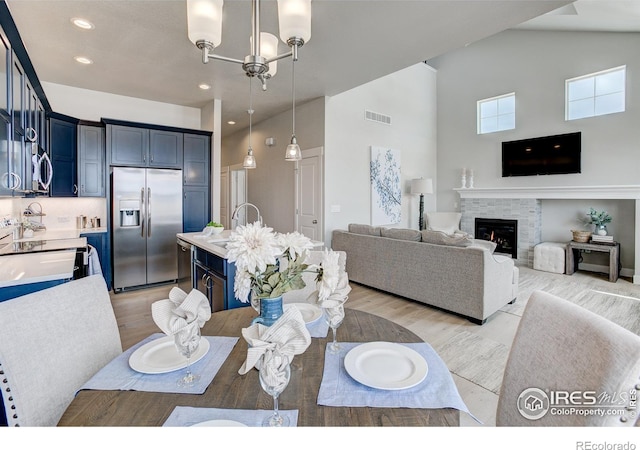 dining room featuring a fireplace, a chandelier, high vaulted ceiling, sink, and light hardwood / wood-style flooring