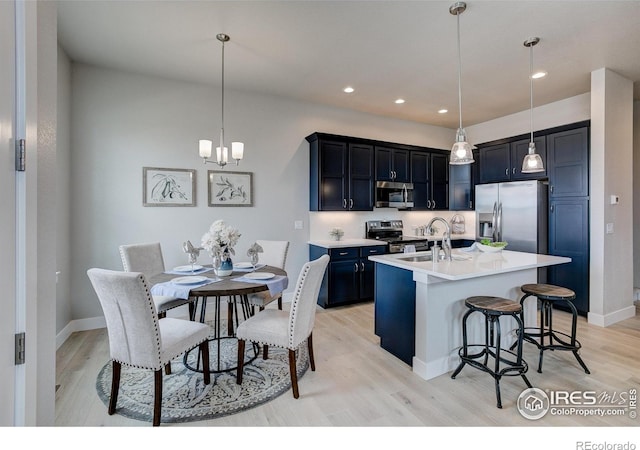 kitchen with appliances with stainless steel finishes, light wood-type flooring, decorative light fixtures, and an island with sink