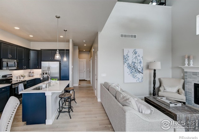 kitchen with appliances with stainless steel finishes, sink, decorative light fixtures, a tile fireplace, and light wood-type flooring