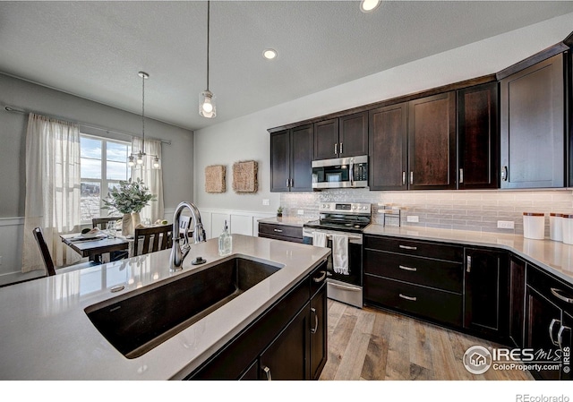 kitchen with tasteful backsplash, light wood-type flooring, stainless steel appliances, hanging light fixtures, and sink