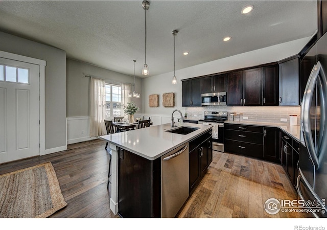 kitchen with stainless steel appliances, hardwood / wood-style floors, sink, decorative light fixtures, and an island with sink