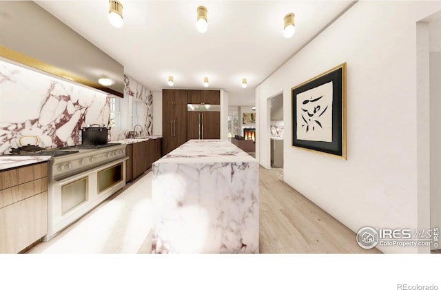 kitchen featuring gas range oven, light wood-type flooring, exhaust hood, a center island, and paneled built in refrigerator