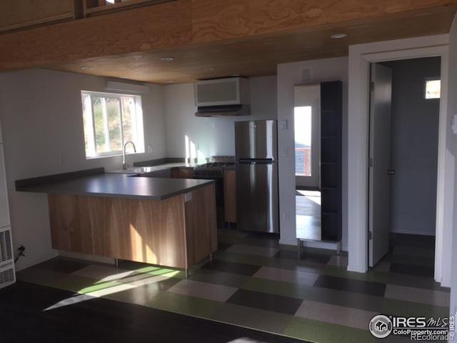 kitchen with kitchen peninsula, exhaust hood, range, stainless steel fridge, and sink