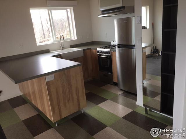 kitchen with stainless steel refrigerator, kitchen peninsula, white range with gas cooktop, wall chimney exhaust hood, and sink