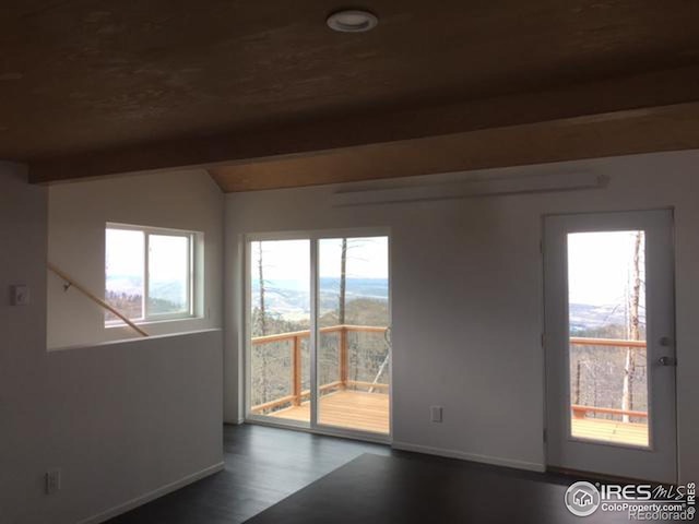 empty room with a wealth of natural light, dark wood-type flooring, and lofted ceiling with beams