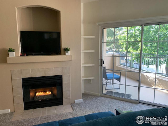 unfurnished living room with built in shelves, a tiled fireplace, carpet flooring, and baseboards