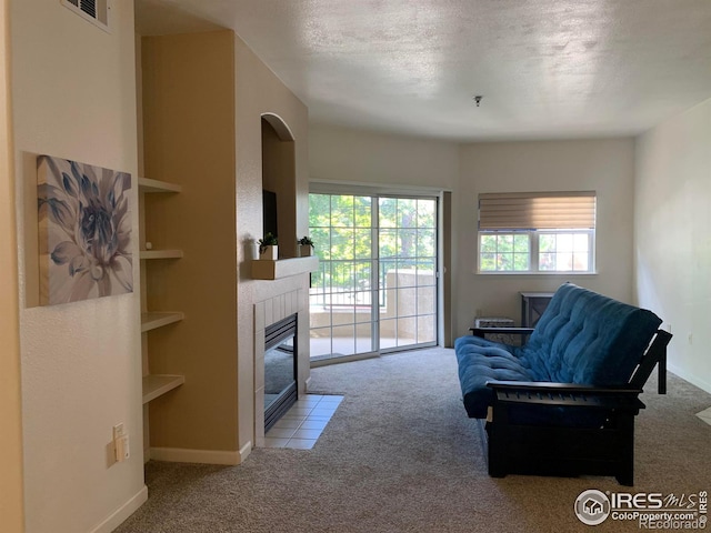 carpeted living area with built in shelves, visible vents, a textured ceiling, a tile fireplace, and baseboards