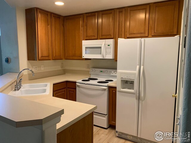 kitchen featuring brown cabinets, light countertops, a sink, white appliances, and a peninsula