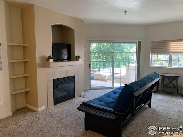 living room featuring a tiled fireplace, built in shelves, carpet, and baseboards